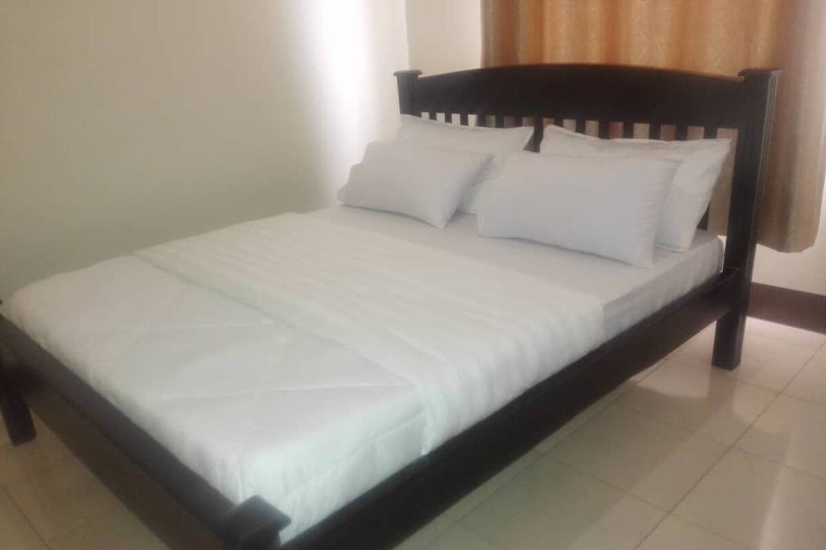 A bed with a white mattress and pillows, a wooden headboard, and a tiled floor.