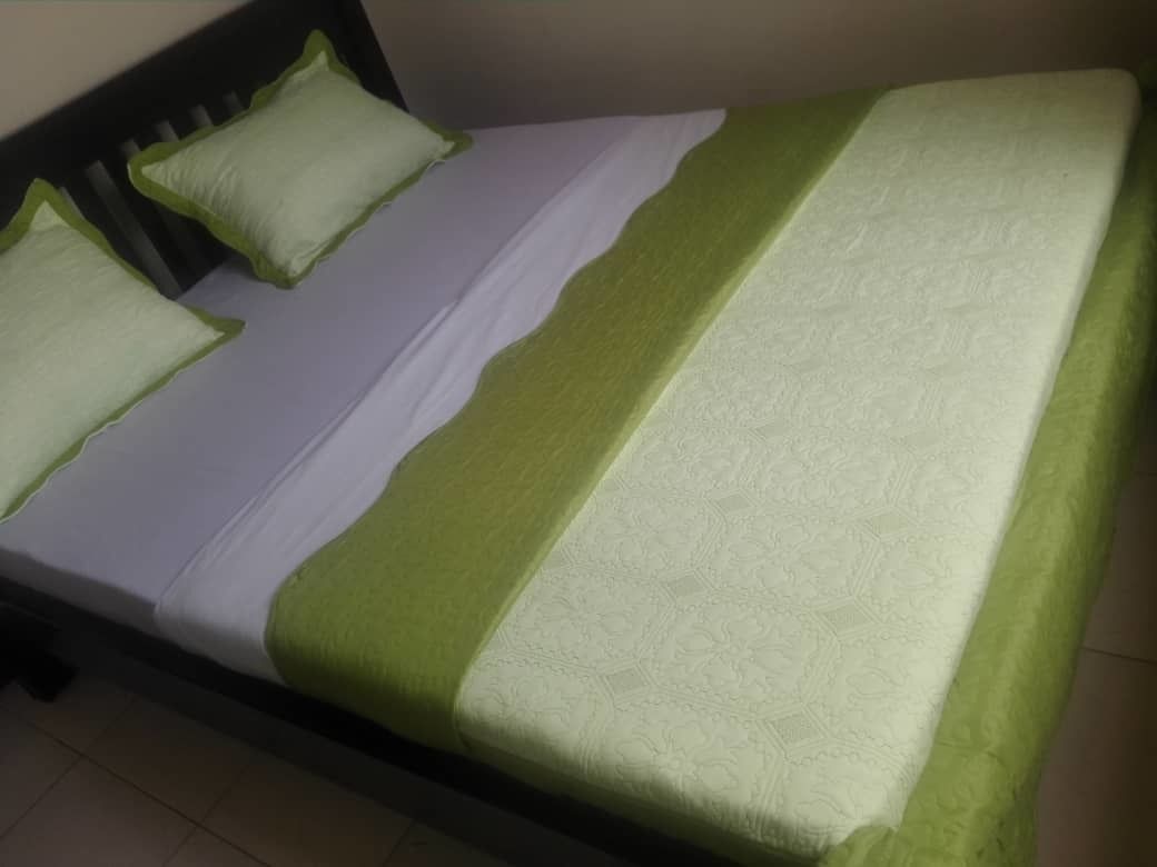 A bed with a green and white bedspread and two pillows.