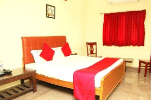 A hotel room with a large bed, a wooden nightstand, a chair, and a red curtain. - Star Residency (Tiruchirappalli)