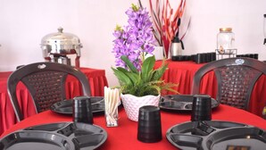 Une table à manger dressée avec des assiettes noires, une plante en pot aux fleurs violettes et un porte-serviettes blanc.