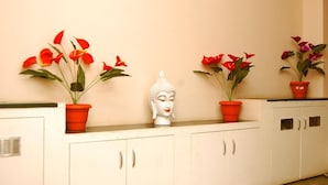 Une pièce avec un meuble blanc, une statue de Bouddha et des fleurs rouges dans des pots rouges.
