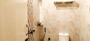 A bathroom with a marble wall, a toilet, a shower with a handheld showerhead, and a towel rack. - Star Residency (Tiruchirappalli)
