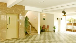 Un hall d’hôtel avec un sol à carreaux, un escalier, deux chaises, une statue de Bouddha et une plante en pot.