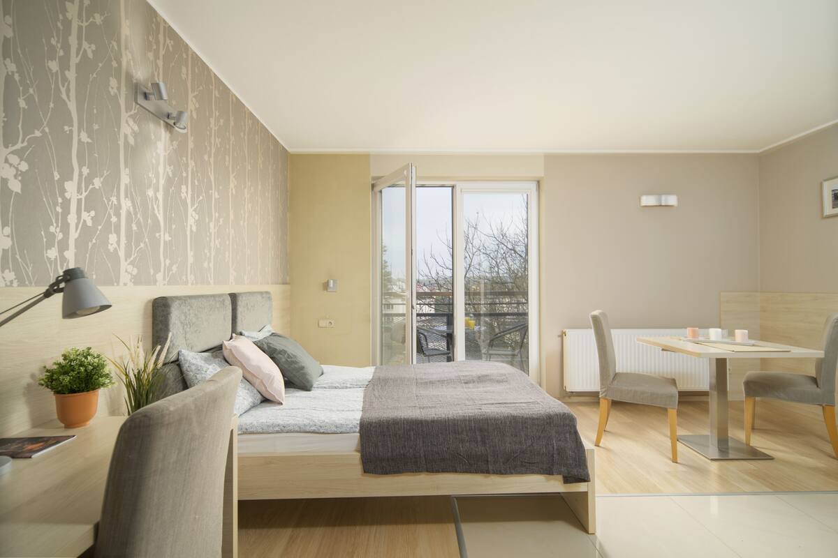 A modern bedroom with a bed, a desk, a chair, and a potted plant.