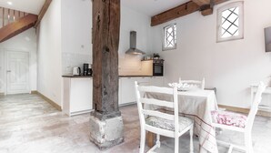 A kitchen with white cabinets, a wooden beam ceiling, and a dining area with white chairs and a table. - Beautiful apartment "chicken coop" in the countryside (Harrierwurp)