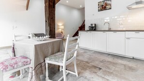 A modern kitchen with white cabinets, a wooden beam ceiling, and a dining area with a table and chairs. - Beautiful apartment "chicken coop" in the countryside (Harrierwurp)