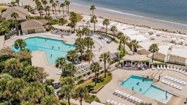 An aerial view of a resort with multiple swimming pools, sun loungers, and palm trees. - Pet Friendly 3BR Tarpon Pond Cottage! Close to Beach/Pools (Seabrook Island)