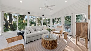 A spacious room with a white ceiling fan, large windows, a beige sofa, a round wooden coffee table, and a wooden easel. - Pet Friendly 3BR Tarpon Pond Cottage! Close to Beach/Pools (Seabrook Island)