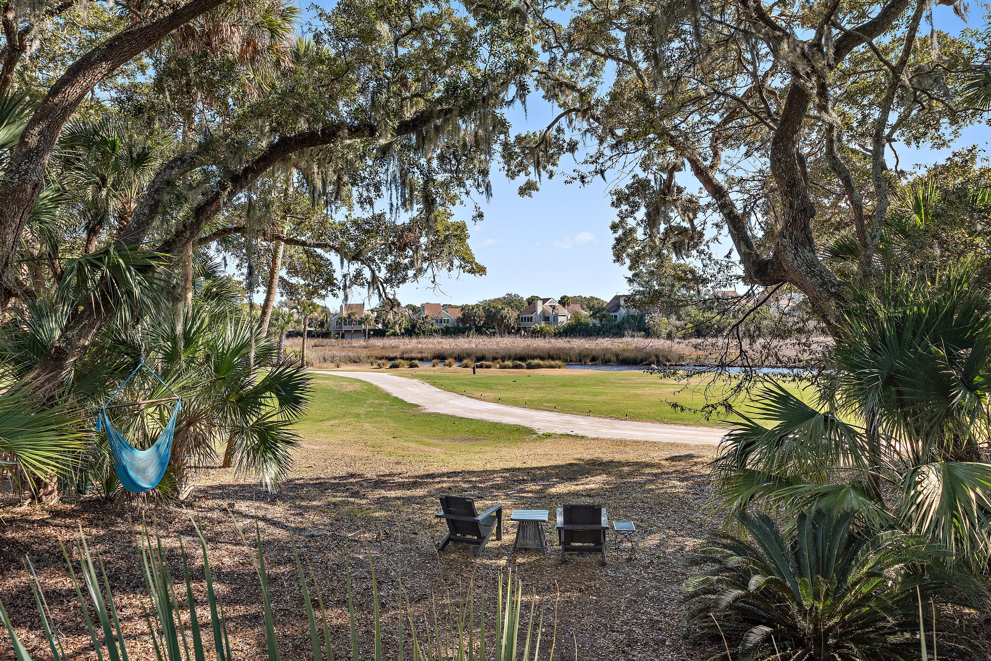 A hammock, two chairs, and a table in a park with a golf course in the background.