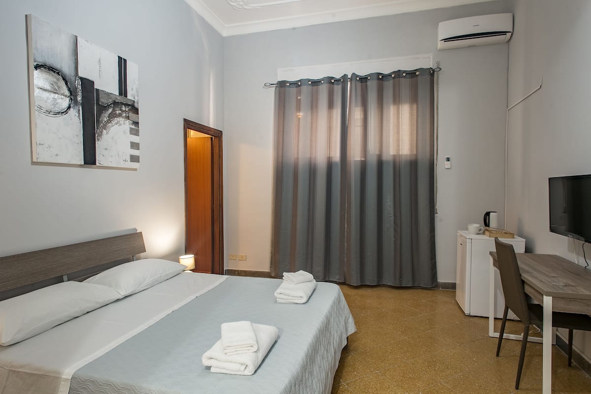 A hotel room with a bed, a desk, a chair, a television, and a curtain.