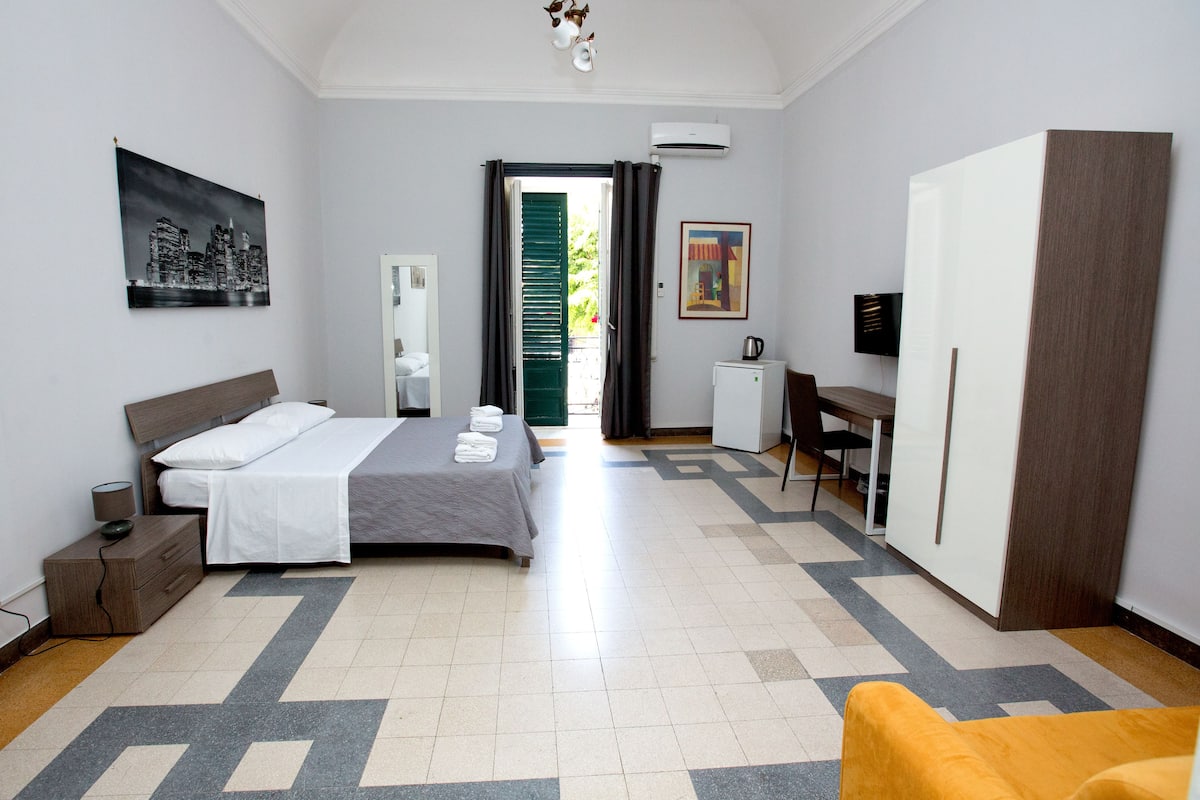 A hotel room with a bed, a desk, a wardrobe, and a television.