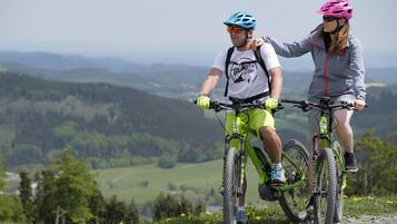 Two people on bicycles on a gravel path with a scenic view of hills and fields.