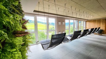 Una habitación con una fila de sillas frente a un amplio ventanal con vistas a un paisaje verde.