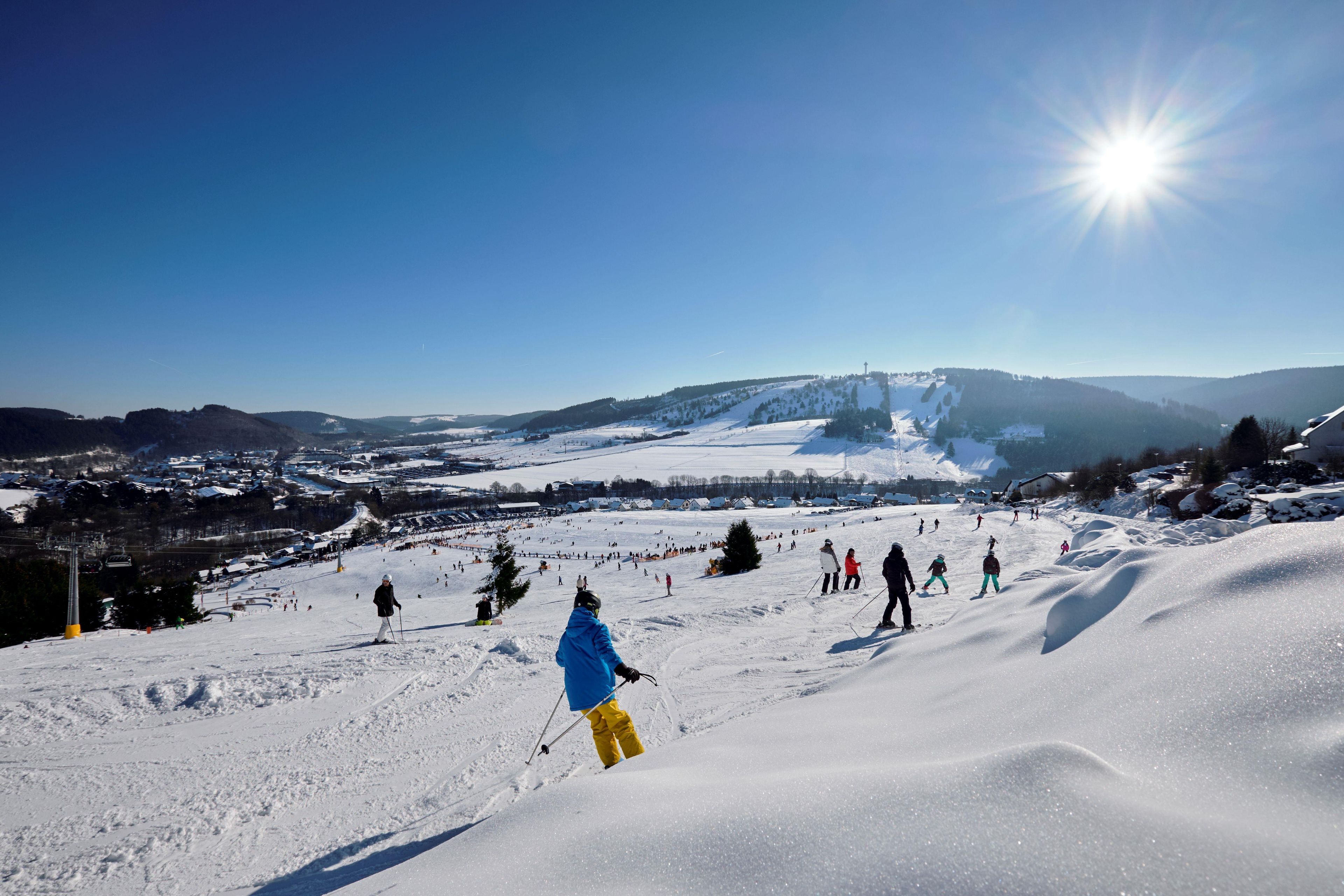 A snowy ski slope with skiers and a clear sky.