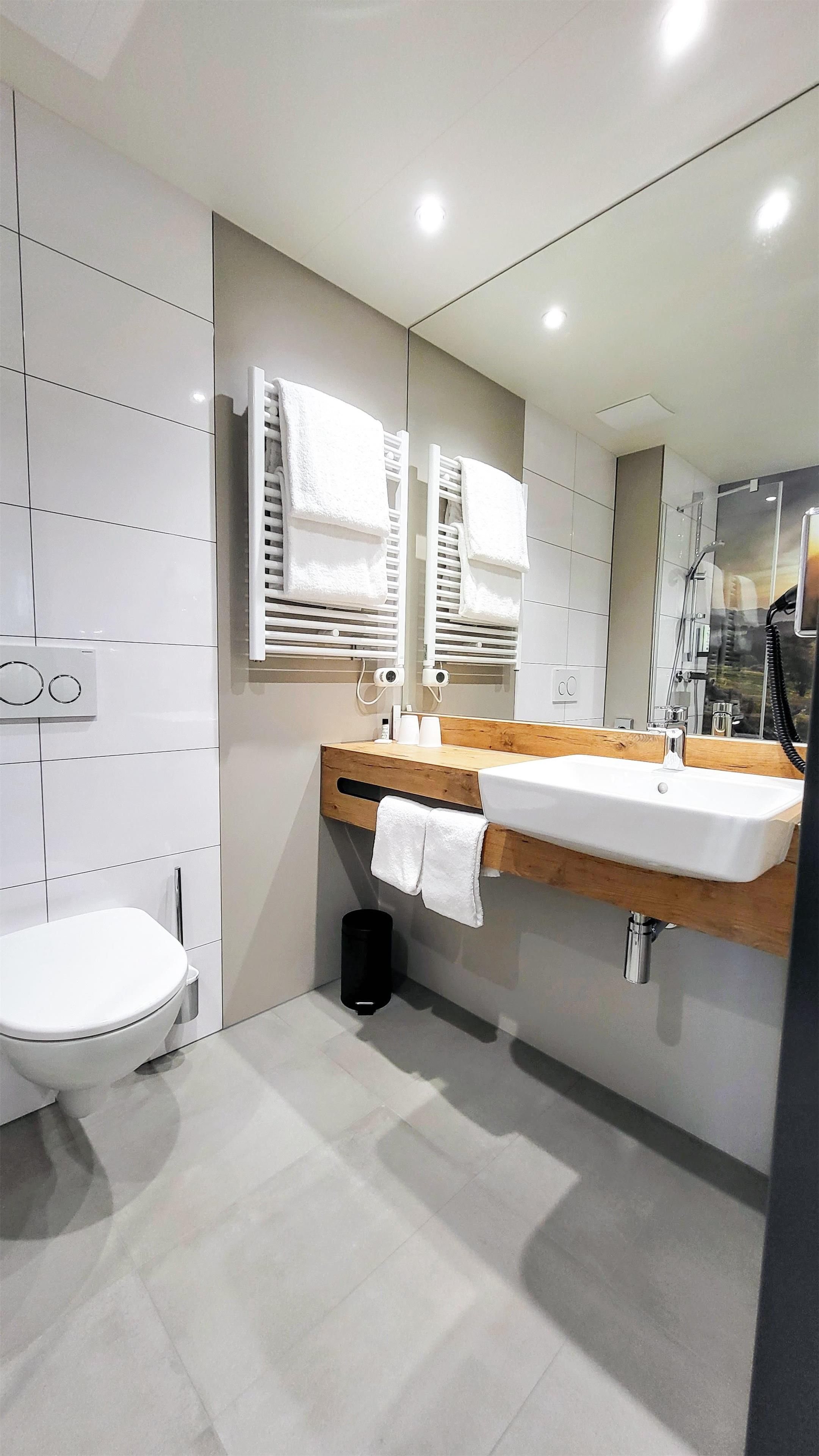 Ein modernes Badezimmer mit einer weißen Toilette, einem Holzwaschtisch mit einem Becken und einem Spiegel darüber.