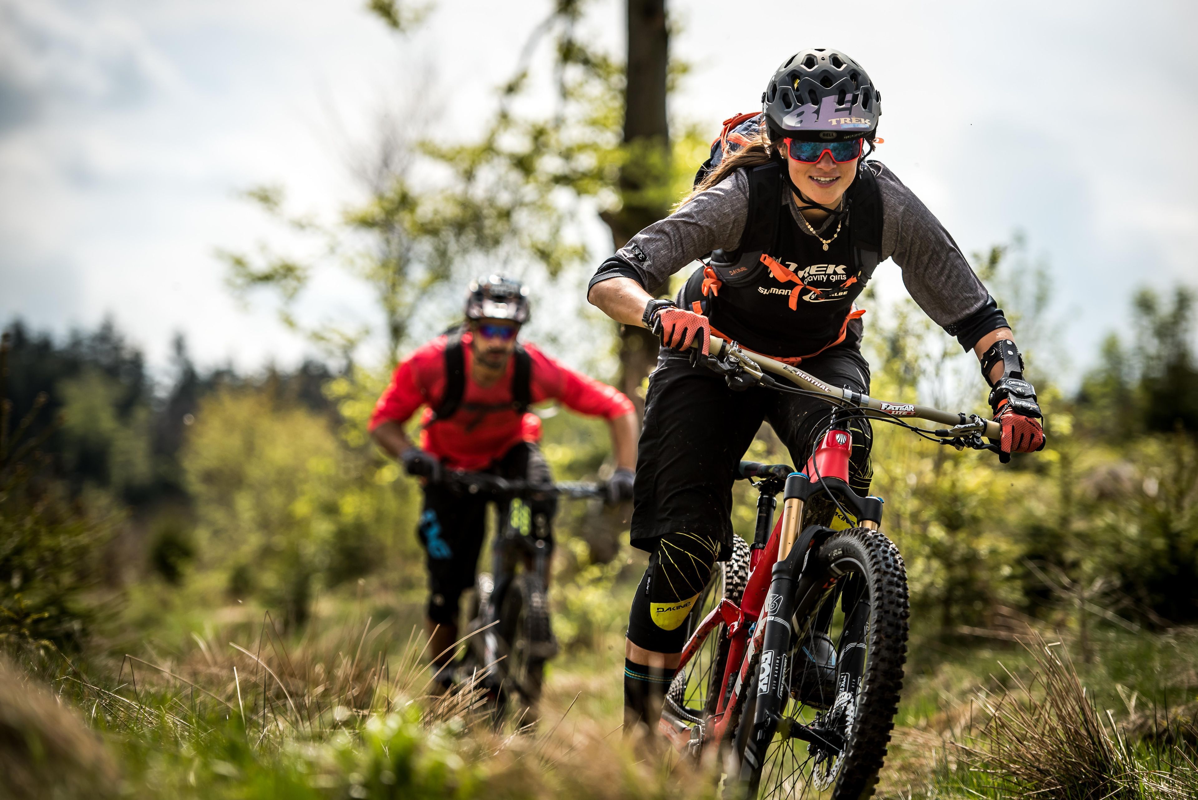 Two mountain bikers on a trail with trees in the background.