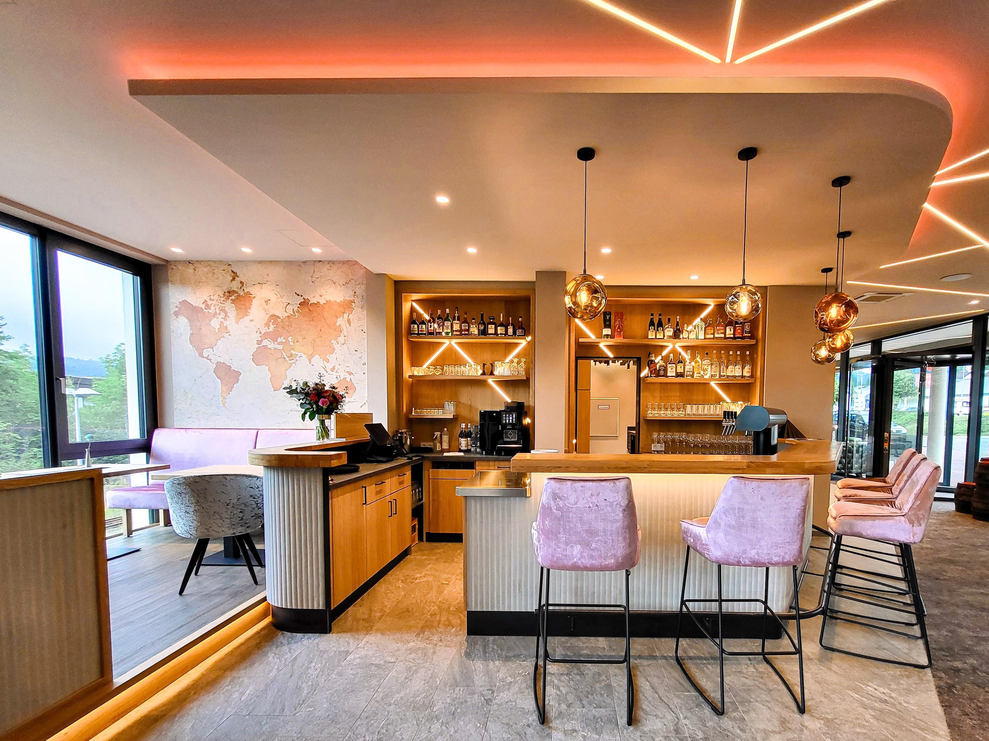 A modern bar area with a world map on the wall, bar stools, and a variety of bottles.