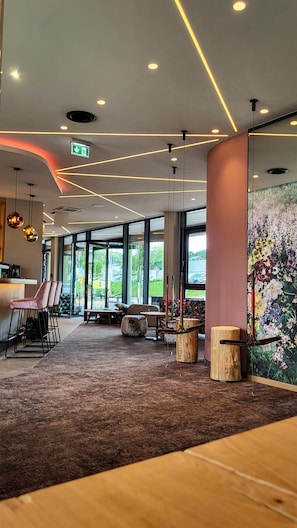 Un intérieur moderne avec un bar, des espaces pour s’asseoir et de grandes fenêtres.