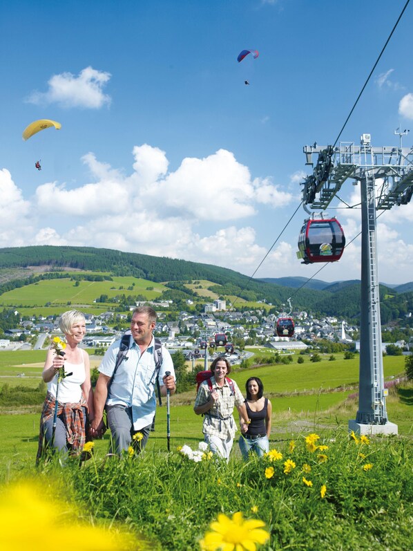 A group of people walking in a grassy area with a cable car in the background. - Mountain View Hotel Willingen, BW Signature Collection (Willingen)