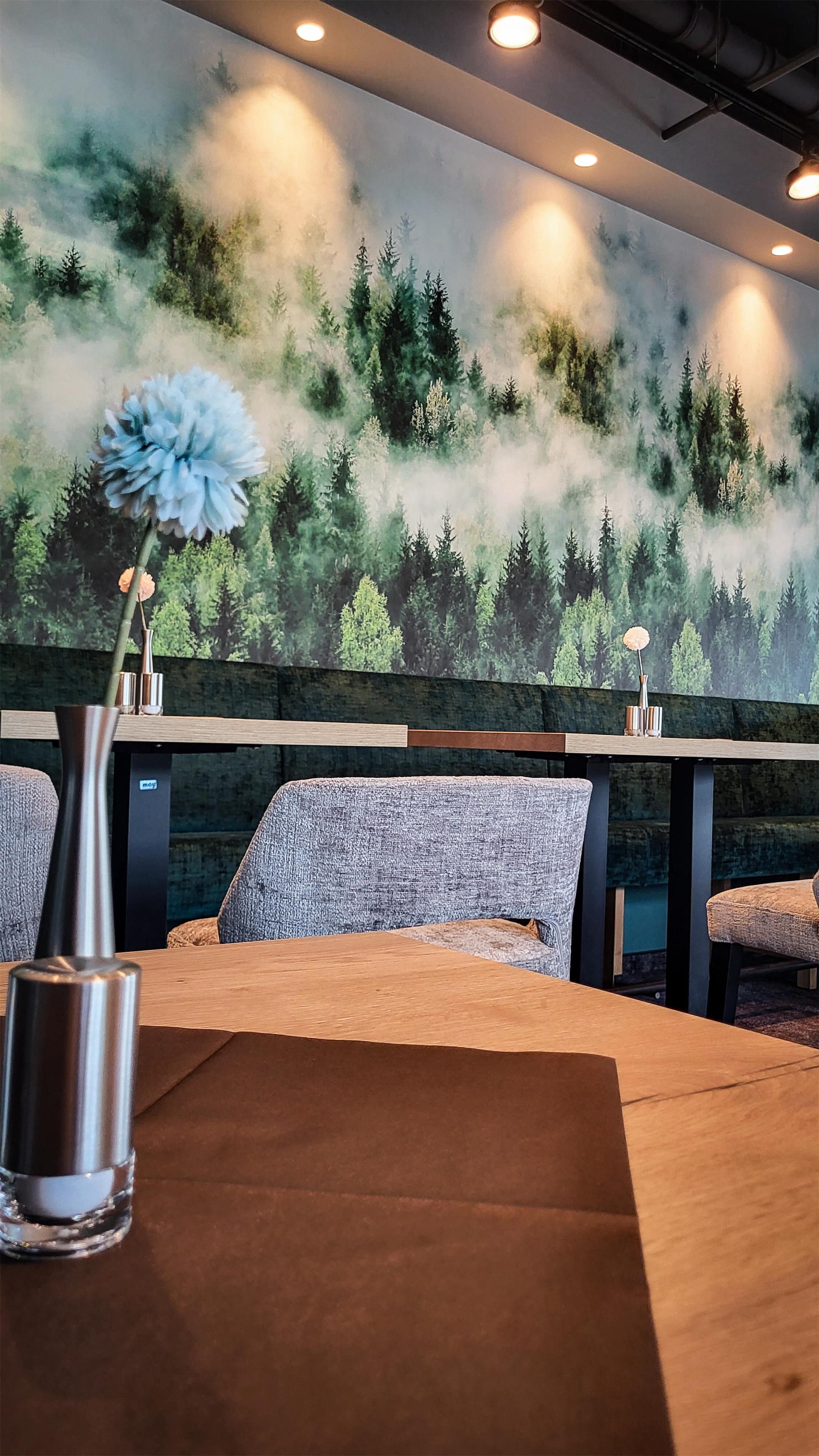 Interior de restaurante con un mural de un bosque, mesas y sillas de madera.