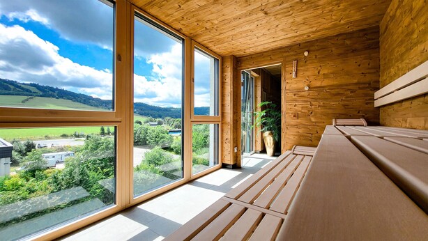 Un intérieur en bois agrémenté de grandes fenêtres qui offrent une vue sur un paysage verdoyant et des bâtiments éloignés.