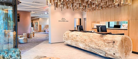 Un espace d’accueil moderne avec un comptoir de réception en bois, des sièges et une grande fenêtre.