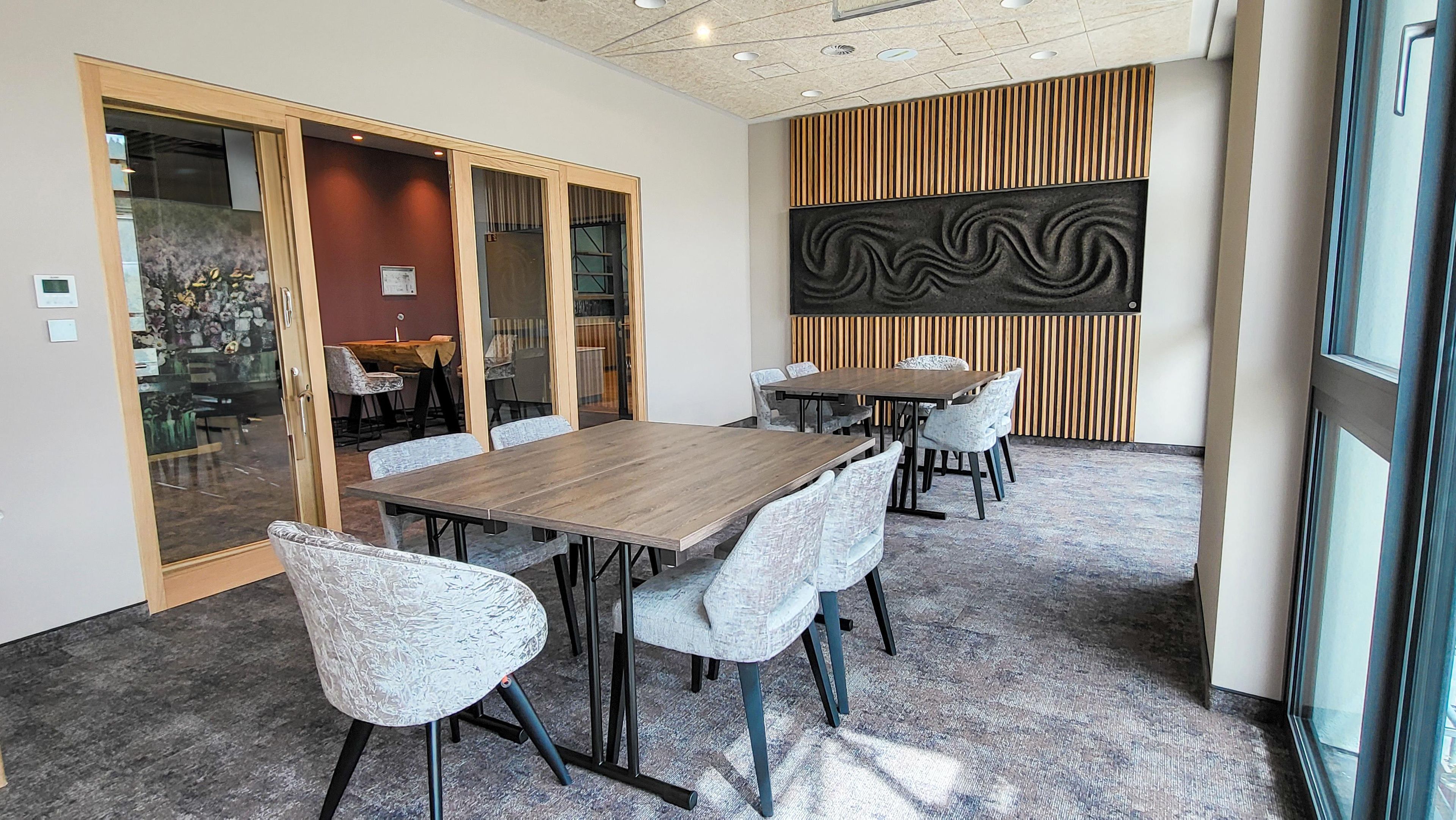 Un salón de conferencias con una gran mesa, sillas, paredes de vidrio y una obra de arte moderna en la pared.