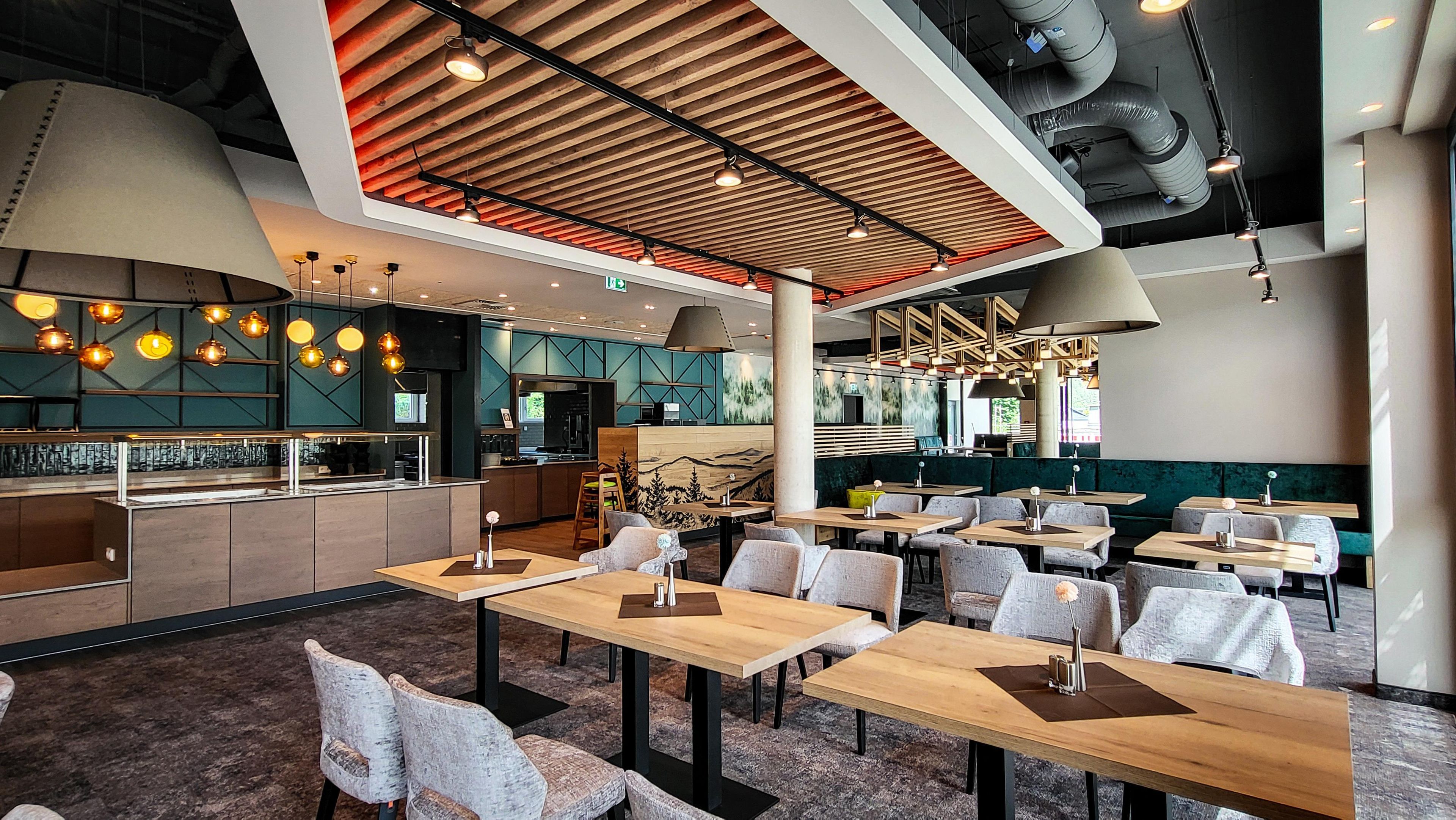 Een modern restaurantinterieur met hoge plafonds, blootgelegde ventilatiekanalen en een combinatie van zitplaatsen, waaronder tafels en zitjes.