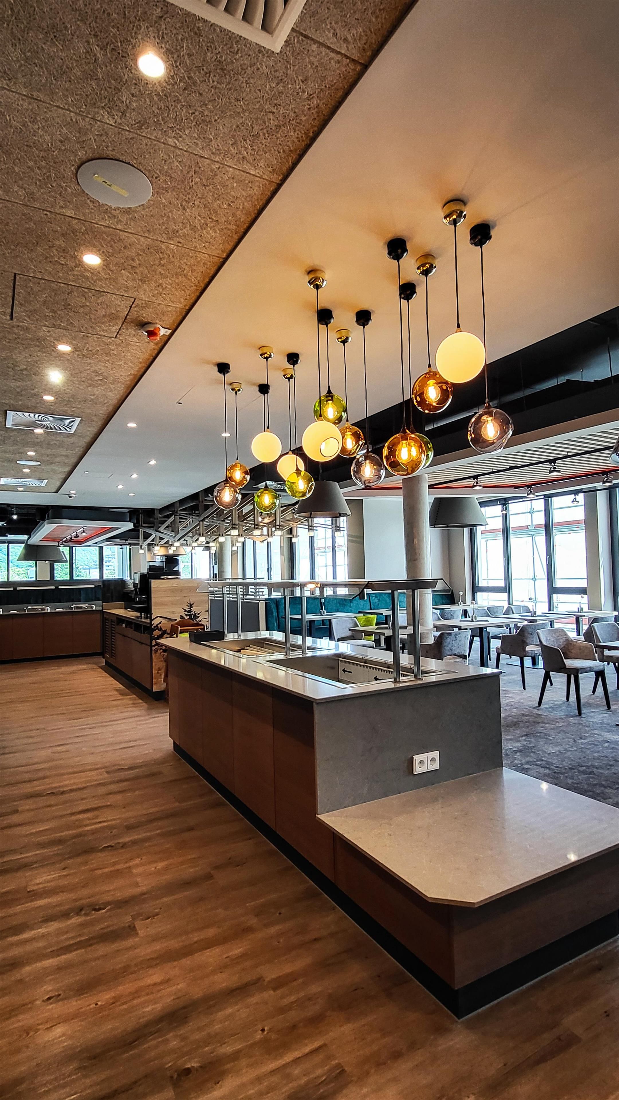 A modern restaurant interior with a central island, multiple hanging pendant lights, and a wooden floor.