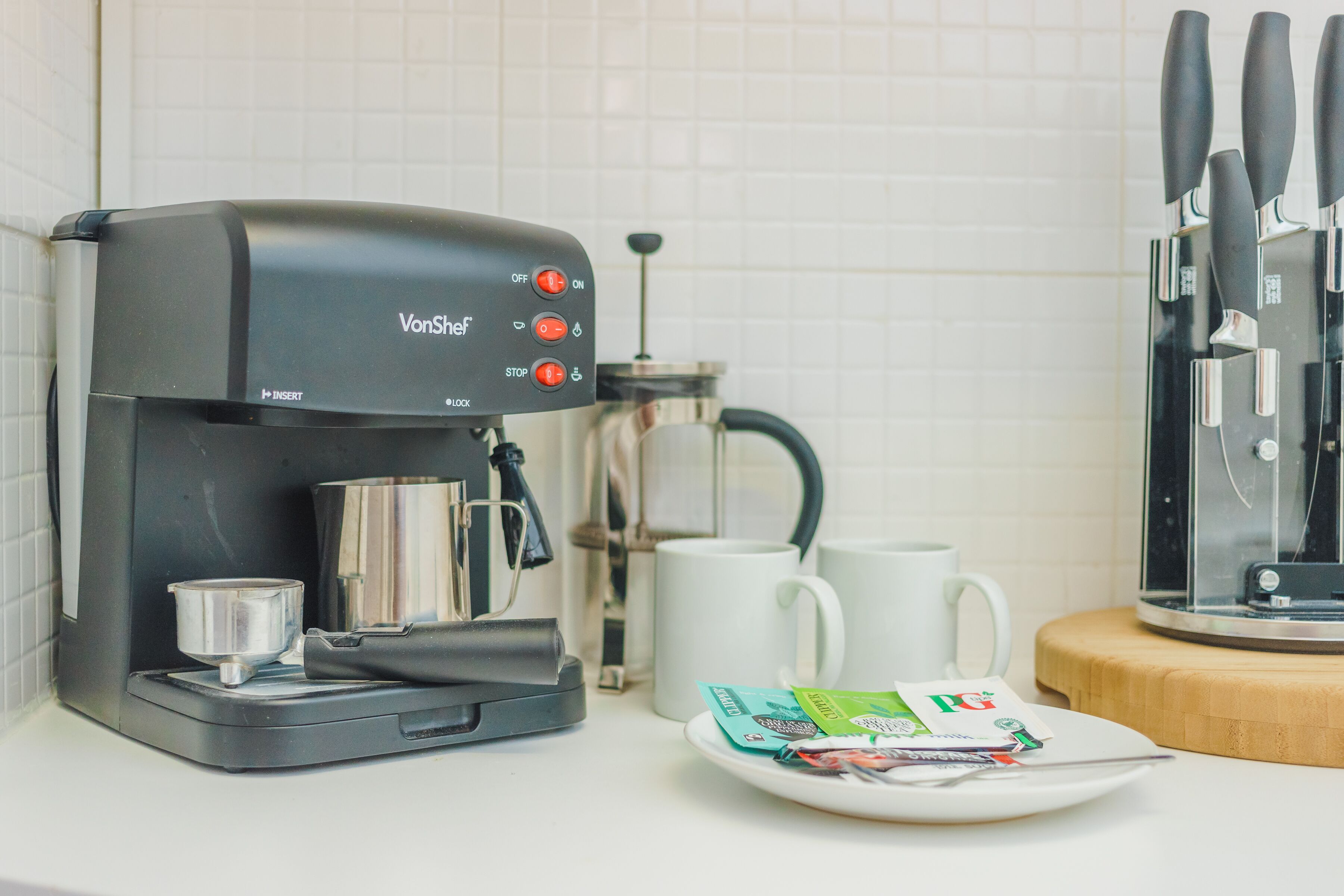 A coffee maker with a control panel, a coffee pot, a white mug, and a plate with coffee pods.