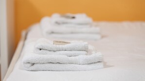 Un montón de toallas blancas ordenadas sobre una cama con un cabecero blanco sencillo y una pared naranja uniforme al fondo.