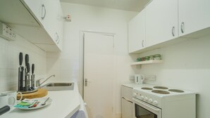 Una cocina con armarios blancos, estufa, lavamanos y cafetera.