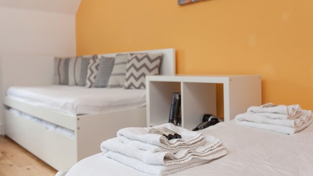 Una cama bien hecha con almohadas, una mesita de noche con libros y una obra de arte en la pared.