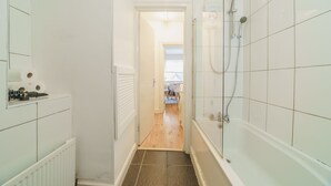 Un baño estrecho con azulejos blancos, ducha y radiador.