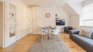 Una sala de estar moderna con comedor, un sofá gris, un televisor y un reloj en la pared.
