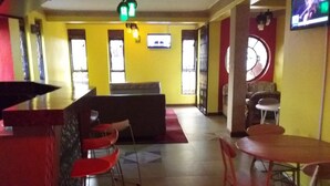 A restaurant with a bar area, red chairs, and a TV screen. - Egret Pilgrims Inn (Kampala)