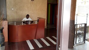 A reception desk with a person seated behind it, a striped floor, and a door leading to a hallway. - Egret Pilgrims Inn (Kampala)
