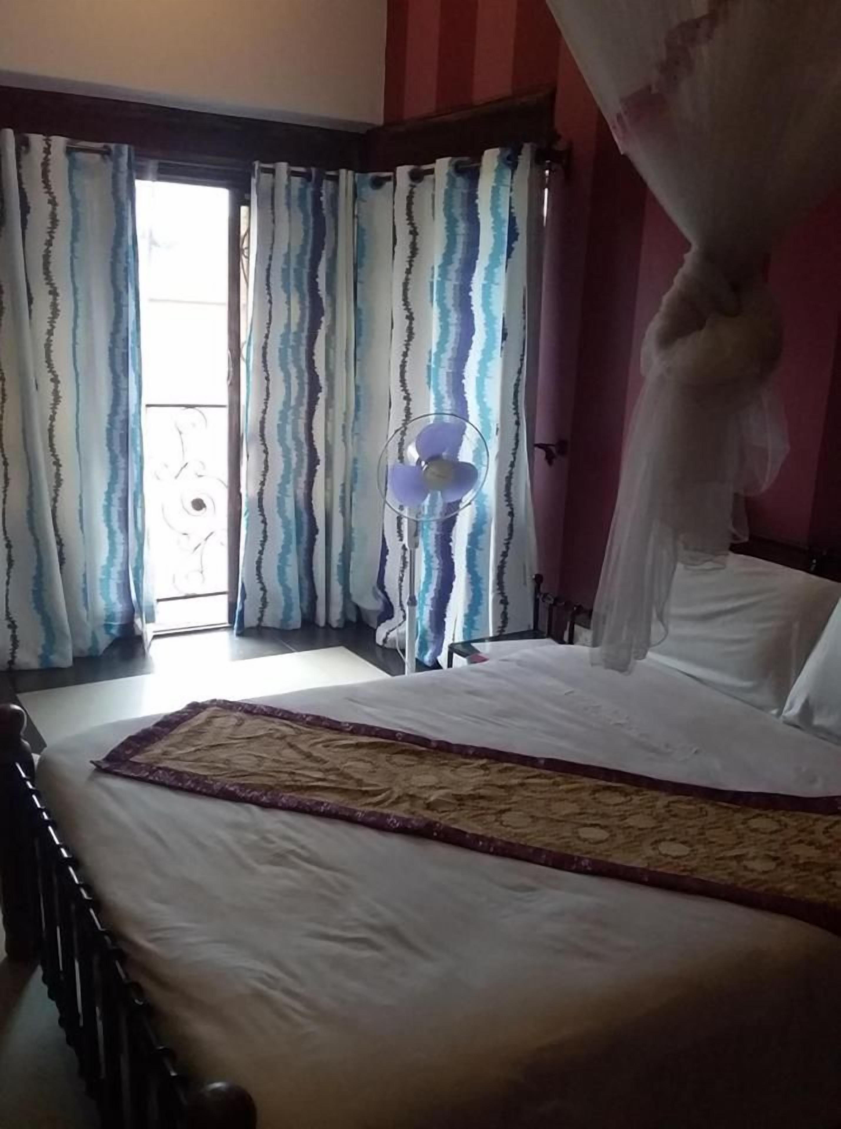 Een slaapkamer met een bed, gordijnen, een ventilator en een raam.