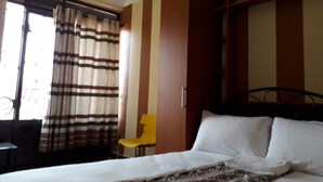 A hotel room with a bed, a chair, and a window with curtains. - Egret Pilgrims Inn (Kampala)