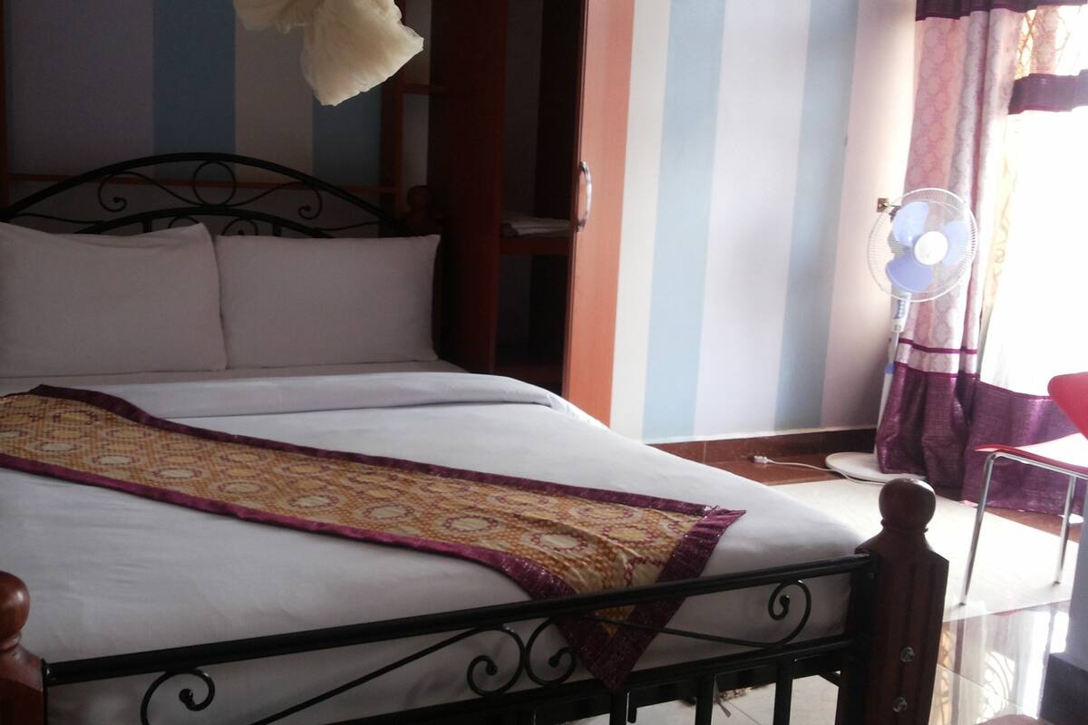 A bed with a patterned bedspread, a bedside table, and a wall fan.