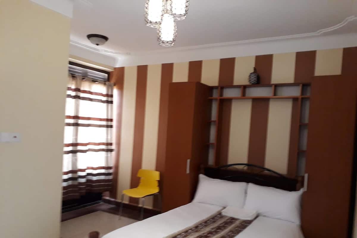A bedroom with a bed, a yellow chair, a ceiling light fixture, and a window with striped curtains.