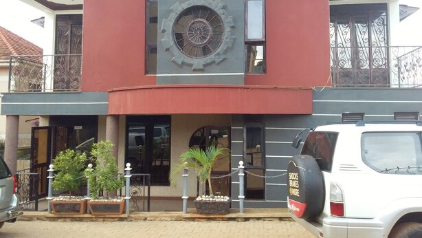 A building with a large clock on the facade, a sign for 'Egrett Pilgrims Inn', and a parked white SUV in front. - Egret Pilgrims Inn (Kampala)