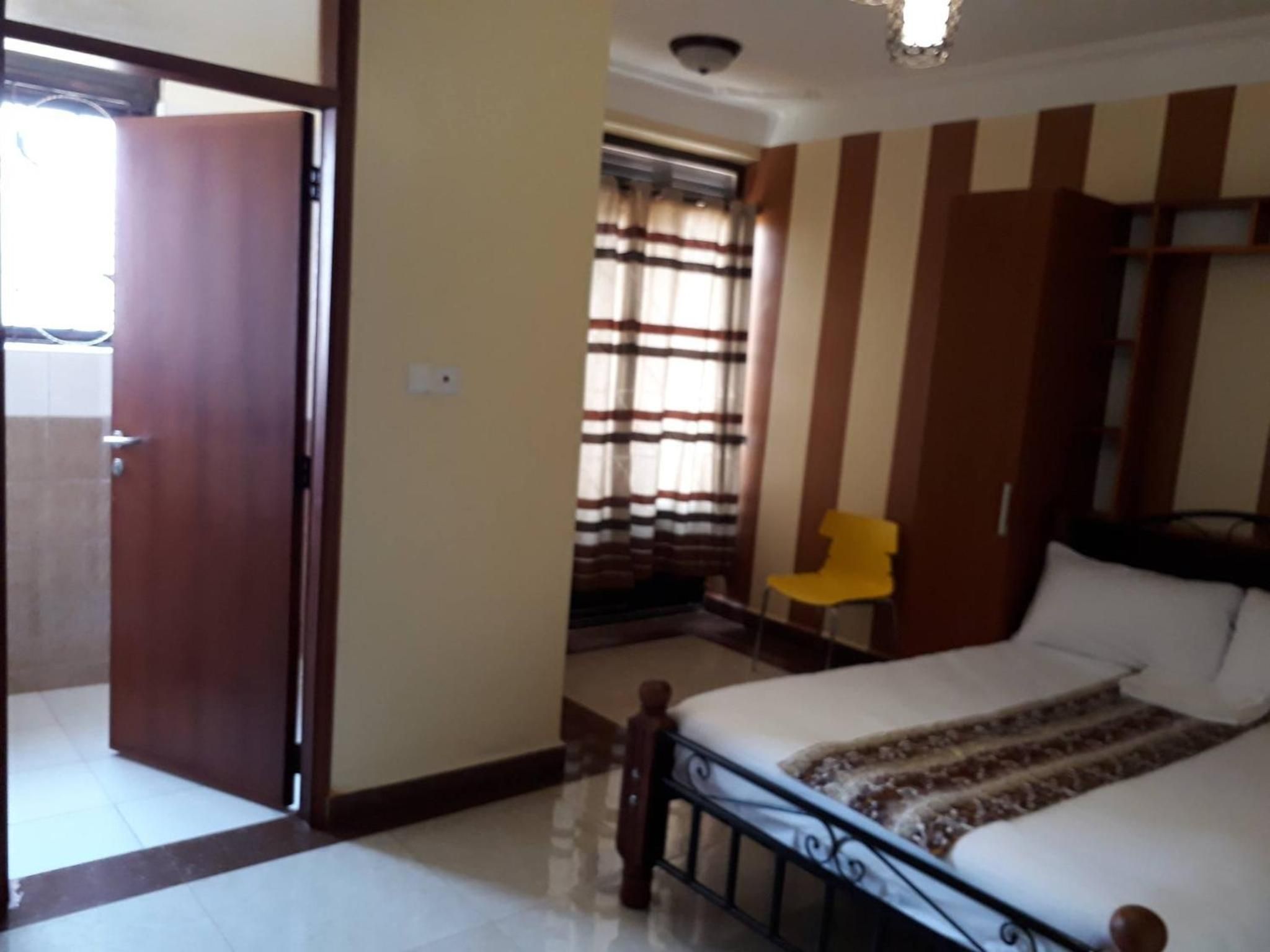 Un dormitorio con cama, una silla, una ventana con cortinas y una puerta.
