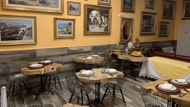 A dining area with multiple tables and chairs, framed artwork on the walls, and a red sofa in the background.