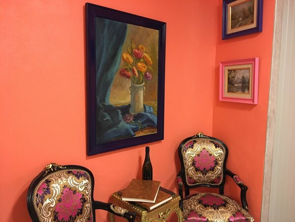 A room with a vibrant orange wall, a framed painting of flowers, two ornate chairs, and a small table with a book. - Musem Spa (Sos del Rey Catolico)