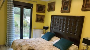 A bedroom with a large bed, a radiator, a window with curtains, and framed pictures on the wall.