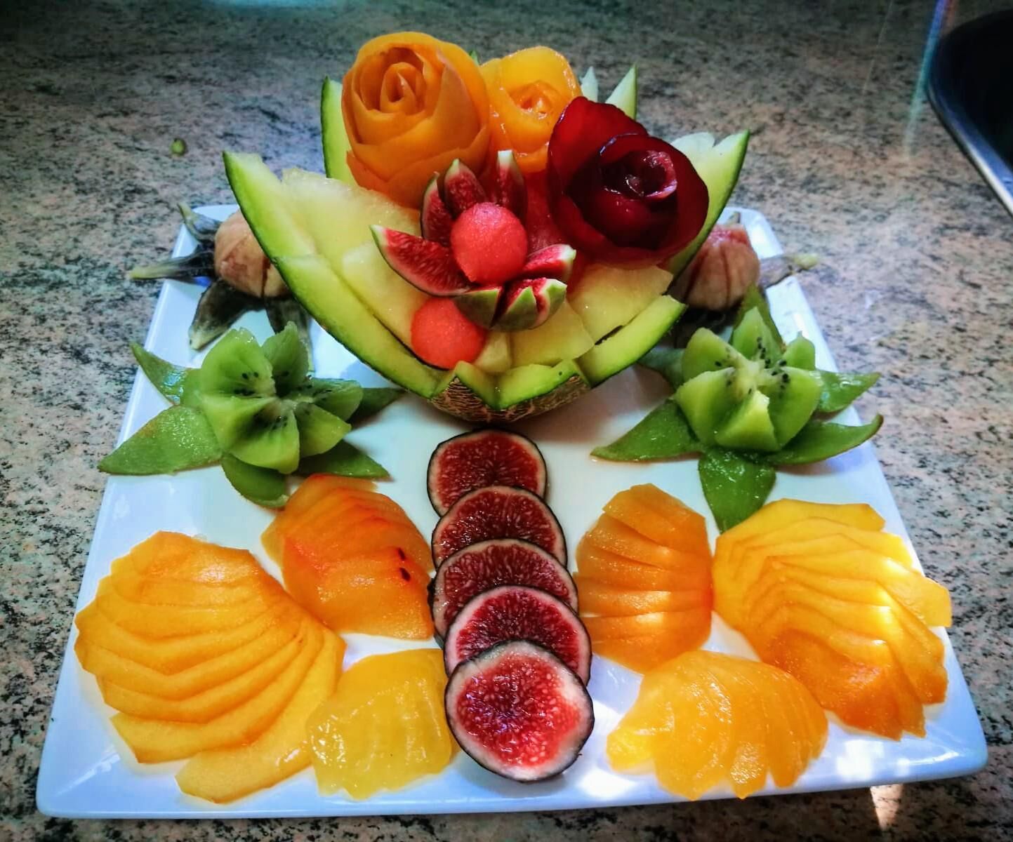 A fruit platter with various fruits arranged on a white plate.