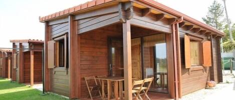 A wooden cabin-style building with a covered patio area, a table, and chairs.