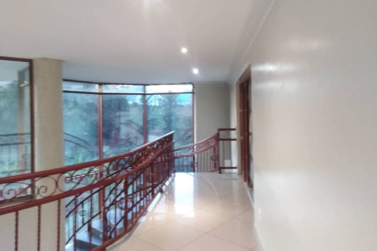 A corridor with a red metal railing, large windows, and a tiled floor.