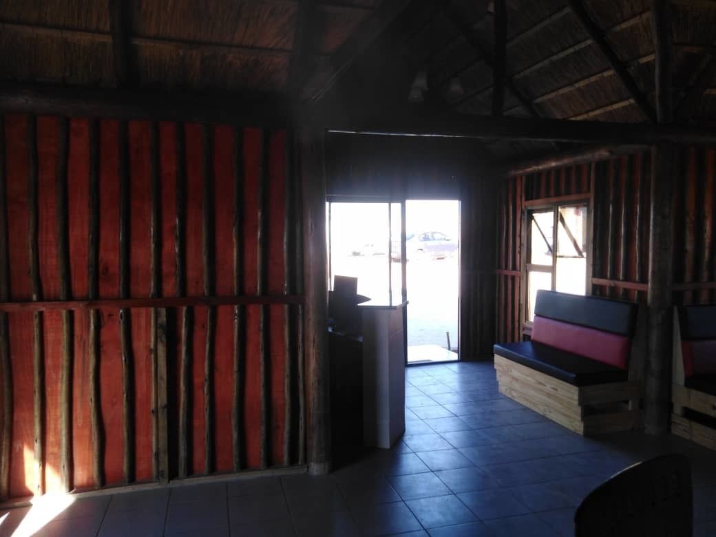A room with a wooden ceiling, a bench with cushions, a tiled floor, and a door leading outside.